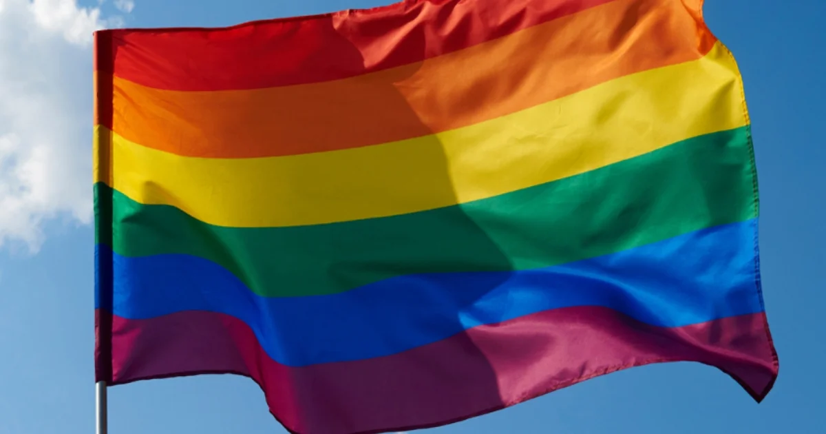 LGBTQ rainbow flag flying against a blue sky